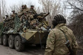 Soldați în uniforme de camuflaj și echipament militar sunt așezați pe un vehicul blindat de transport pe un drum de țară.