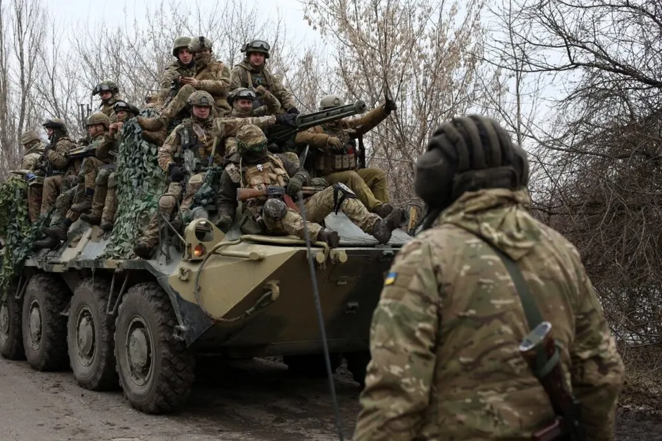 Soldați în uniforme de camuflaj și echipament militar sunt așezați pe un vehicul blindat de transport pe un drum de țară.