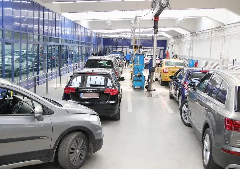 Mai multe mașini sunt parcate într-un atelier de service auto cu podea albă și panouri de sticlă albastră pe lateral.