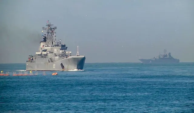 Două nave militare gri navighează pe o suprafață de apă sub un cer senin.