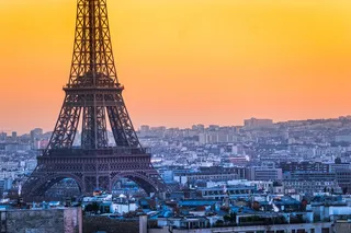 Turnul Eiffel se ridică deasupra unui peisaj urban dens sub un cer de culoare portocalie la apus.