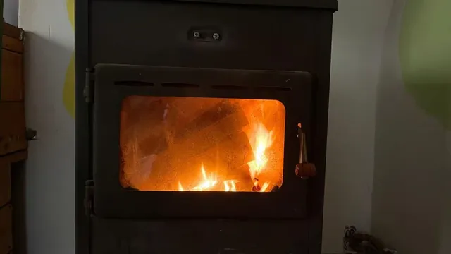 Un foc arde în interiorul unei cuptoare negre cu o fereastră de sticlă transparentă.