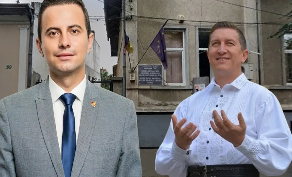 Un bărbat poartă costum gri cu cravată albastră, iar lângă el un alt bărbat poartă o cămașă albă tradițională cu mâneci lungi.