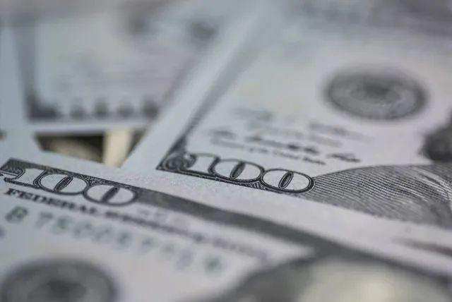Mai multe bancnote de o sută de dolari sunt întinse pe o suprafață plană, prezentând numărul o sută și textul Federal Reserve.