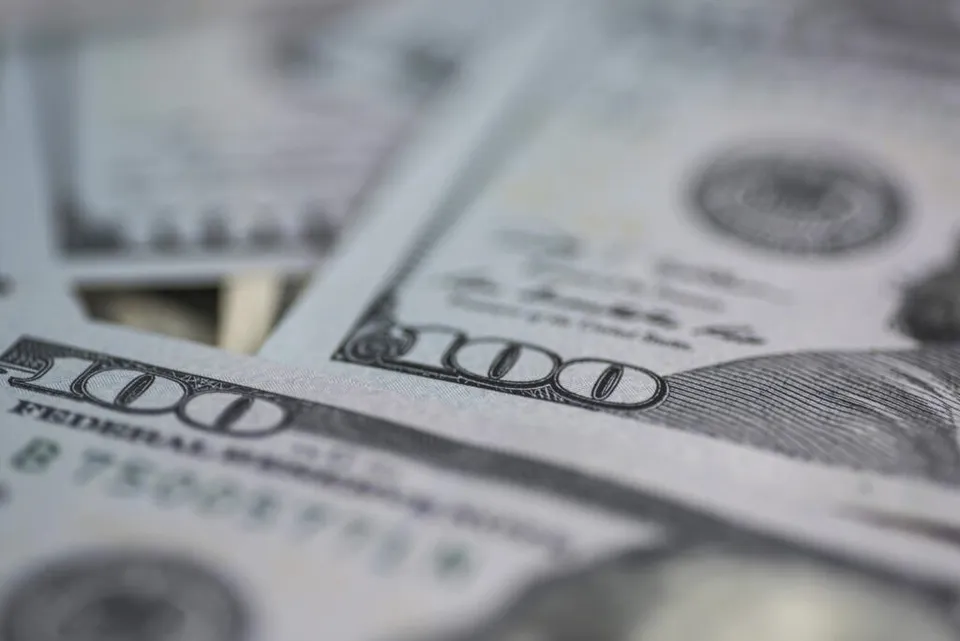 Mai multe bancnote de o sută de dolari sunt întinse pe o suprafață plană, prezentând numărul o sută și textul Federal Reserve.