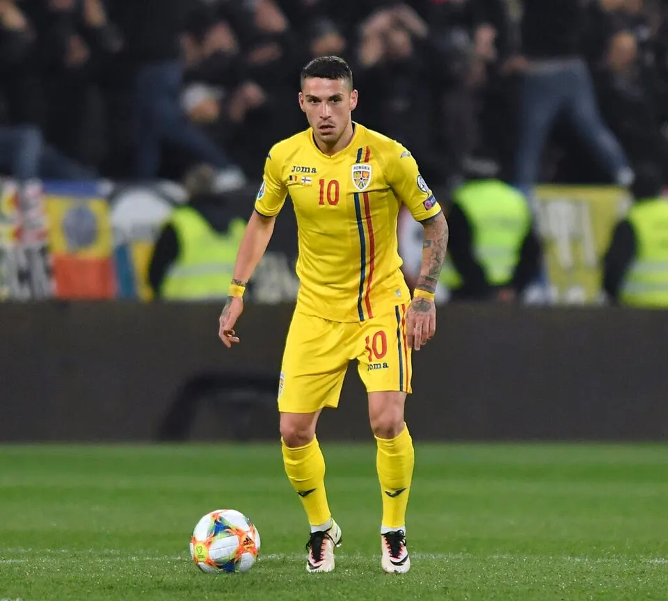 Un fotbalist într-un echipament galben cu numărul zece stă pe un teren de fotbal lângă un balon.