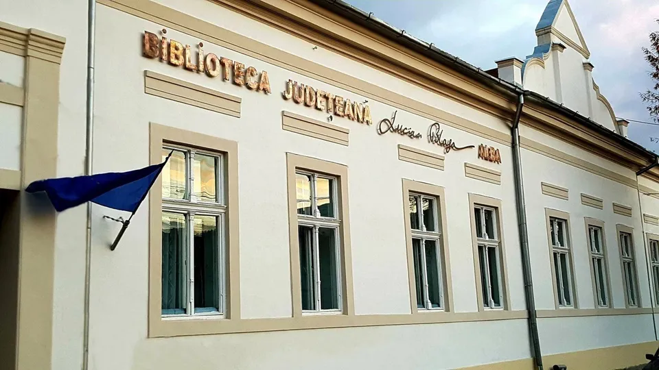 Fațada unei clădiri cu ferestre înalte, inscripție de bibliotecă și un drapel al Uniunii Europene.