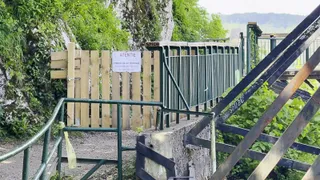 O poartă de lemn închisă cu un anunț, parapet metalic verde și o structură de metal în construcție pe un drum pavat.