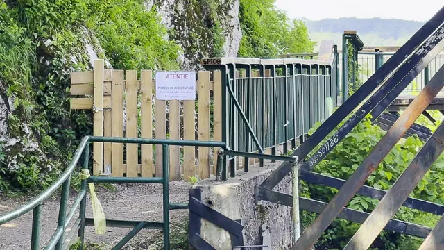 O poartă de lemn închisă cu un anunț, parapet metalic verde și o structură de metal în construcție pe un drum pavat.