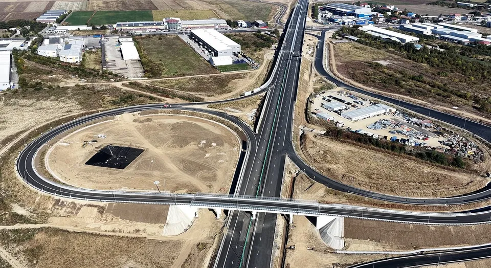 O vedere aeriană prezintă o intersecție de autostradă cu poduri, drumuri asfaltate și terenuri deschise cu vegetație rară.