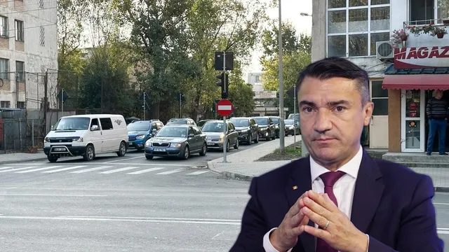 Un bărbat într-un costum închis și cravată purtată într-o poziție de vorbire stă în prim-plan, în fața unui rând de mașini parcate pe stradă.