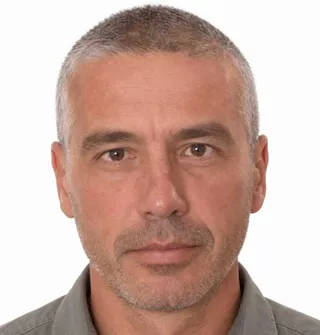 Un bărbat cu părul scurt și cărunt, având barba și mustața scurte, privește spre cameră pe un fundal alb.