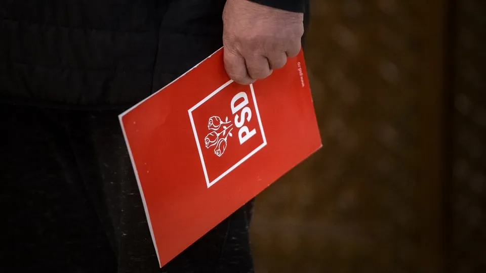 O persoană ține în mână un dosar roșu pe care este imprimat un logo alb cu textul PSD și simboluri grafice.