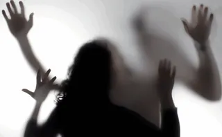 Siluetele întunecate ale unor mâini și capul unei persoane sunt vizibile prin o suprafață mată și albă.