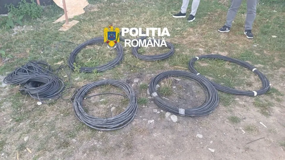 Câteva role de cabluri negre sunt întinse pe un teren cu iarbă și pământ.