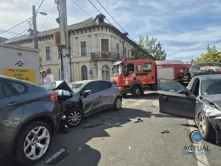 Trei autoturisme și un vehicul de serviciu roșu sunt poziționate pe un drum asfaltat lângă o clădire cu ferestre și balustradă.