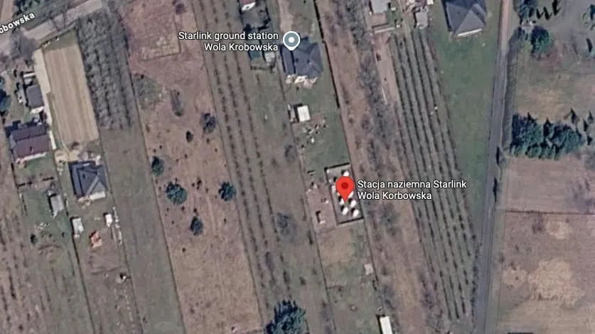 O imagine satelitară arată o zonă rurală cu terenuri, câteva clădiri și un marcaj de locație roșu pe o structură mică.