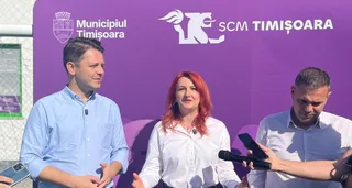 Trei persoane stau în fața unui panou violet pe care sunt afișate logourile Municipiului Timișoara și SCM Timișoara, în timp ce unul dintre ei ține un microfon.