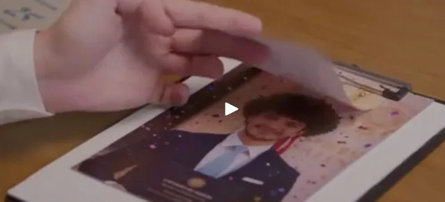 O mână ține o bucată de hârtie deasupra unei fotografii a unui bărbat într-un costum pe un suport de clipboard.
