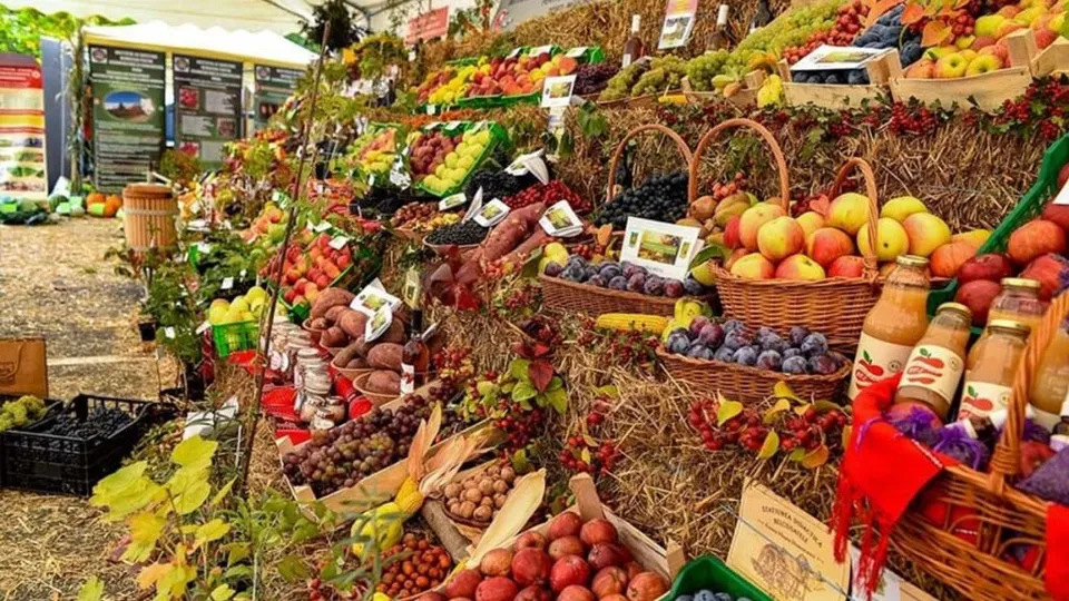 Diverse fructe și legume sunt expuse în coșuri de răchită și pe straturi de paie într-un stand de vânzare în aer liber.