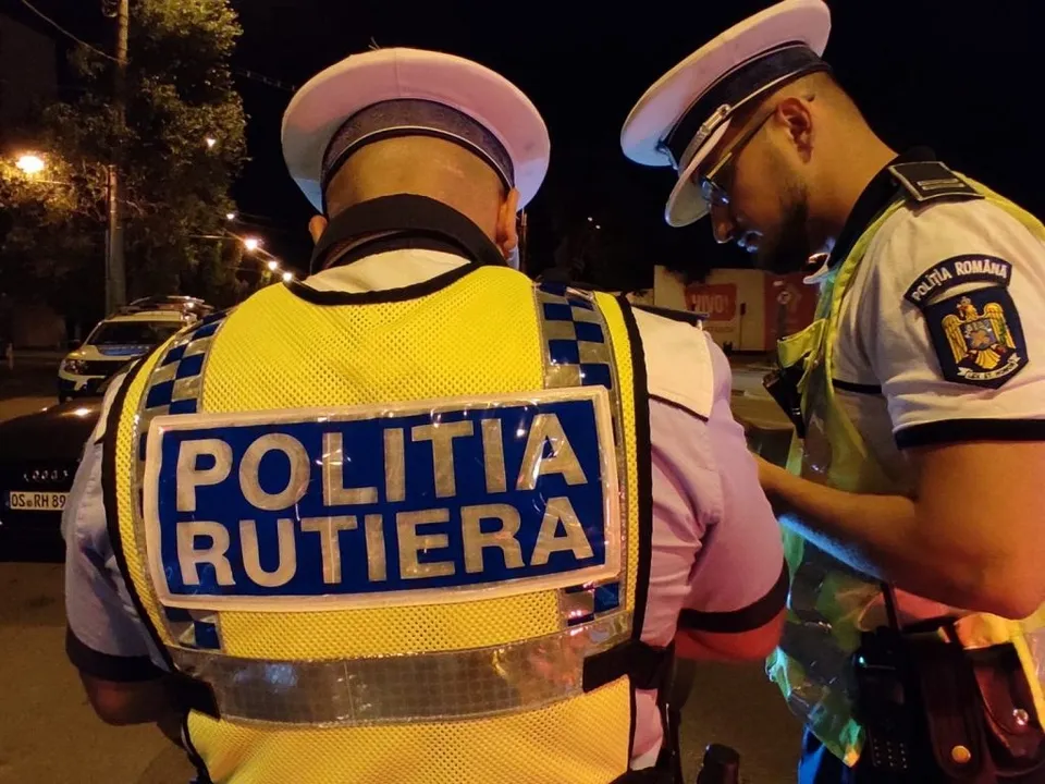 Doi polițiști în uniformă cu vestă reflectorizantă stau pe stradă noaptea.