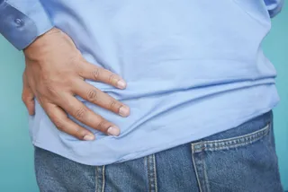 O persoană purtând o cămașă albastră și pantaloni de jean își ține mâna pe zona șoldului.