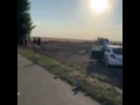 Două autovehicule sunt parcate pe marginea unui drum lângă un câmp sub un cer luminos.