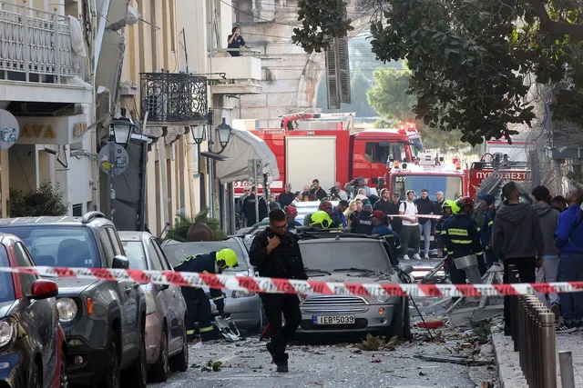 O mulțime de oameni și vehicule de intervenție roșii sunt situate pe un drum strâmt lângă mașini parcate și o zonă delimitată cu bandă de alertă.