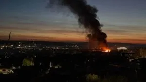 Un nor gros de fum negru se ridică deasupra unui oraș în timpul apusului sau al răsăritului.