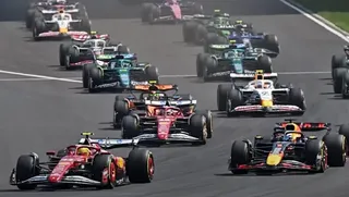 Mai multe mașini de Formula 1 circulă pe un circuit de curse asfaltat.