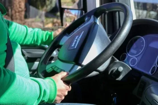 O persoană îmbrăcată într-un hanorac verde ține volanul unui camion aflat în interiorul cabinei.