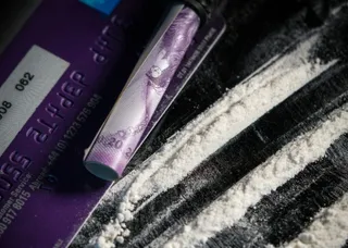 Un tub de carton cu un desen violet este așezat lângă linii de o substanță albă granulară pe o suprafață închisă lângă un card violet.