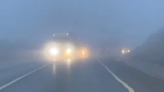 Un vehicul cu farurile aprinse circulă pe un drum asfaltat în condiții de ceață densă.