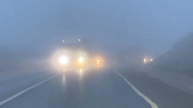 Un vehicul cu farurile aprinse circulă pe un drum asfaltat în condiții de ceață densă.