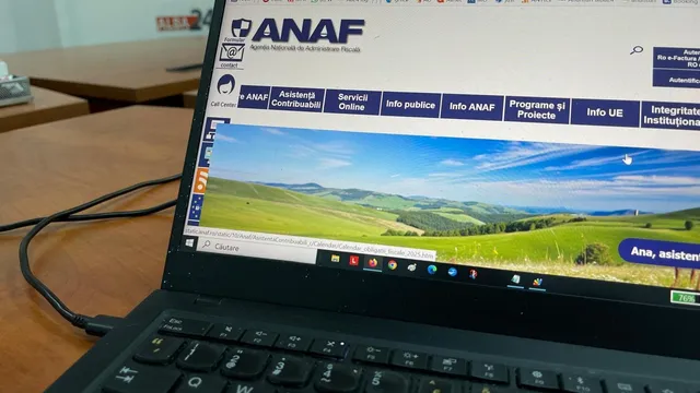 Un laptop deschis afișează un site web cu logo-ul ANAF și o imagine cu dealuri verzi sub un cer albastru.