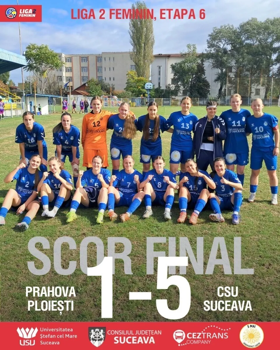 O echipă de fotbal feminin poartă echipamente sportive albastre și portocalii, pozând pe un teren de fotbal verde sub un cer înnorat.