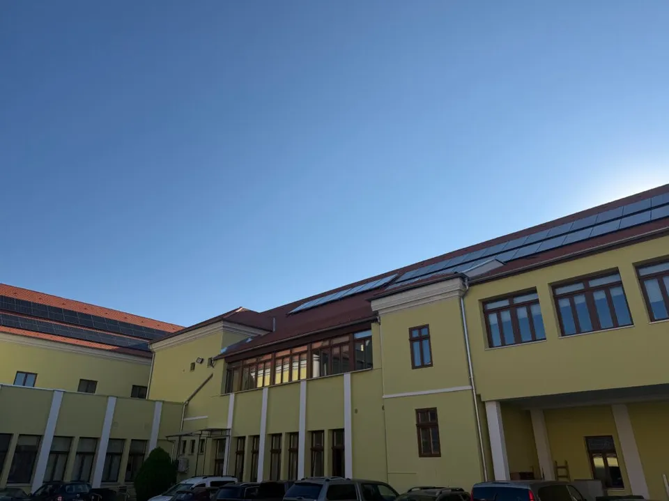 O clădire galbenă cu ferestre și panouri solare pe acoperiș este situată sub un cer senin.