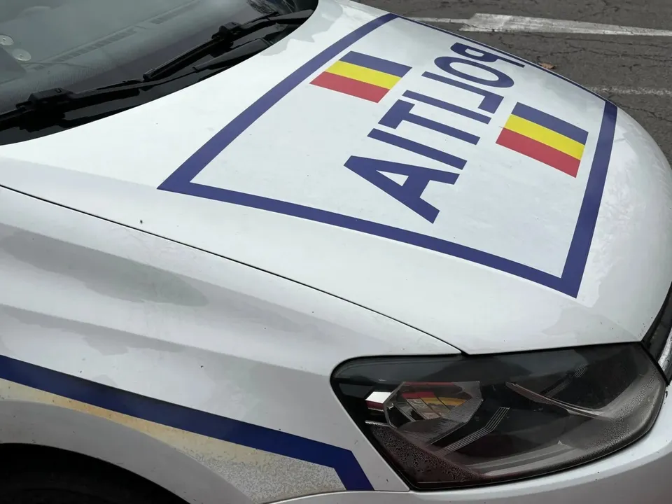 Un capot de mașină alb cu inscripția poliție și culorile drapelului român este vizibil în prim-plan.