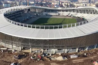 O vedere aeriană a unui stadion mare cu o structură de acoperiș albă și un teren de fotbal verde în interiorul său.