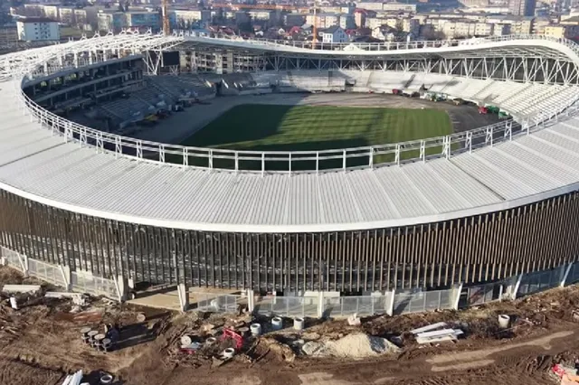 O vedere aeriană a unui stadion mare cu o structură de acoperiș albă și un teren de fotbal verde în interiorul său.