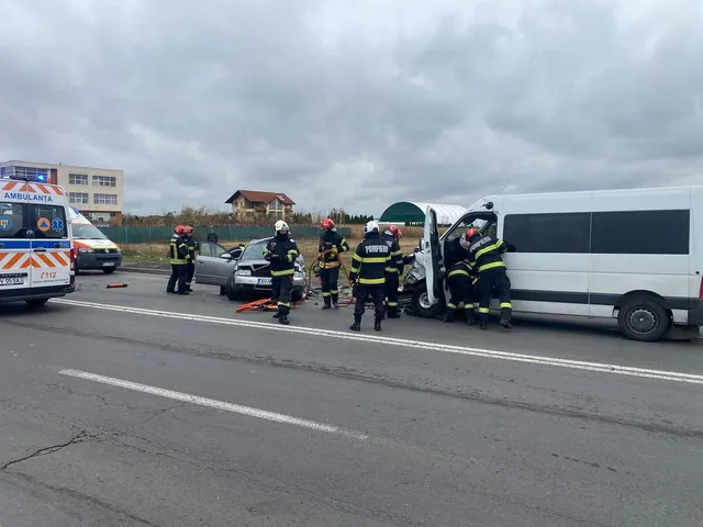 Mai mulți salvatori în uniforme fluorescente lucrează lângă un autoturism gri și un microbuz alb pe o șosea asfaltată sub un cer înnorat.