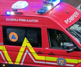Un vehicul de serviciu de culoare roșie prezintă inscripții albe și lumini de semnalizare albastre aprinse pe plafon.