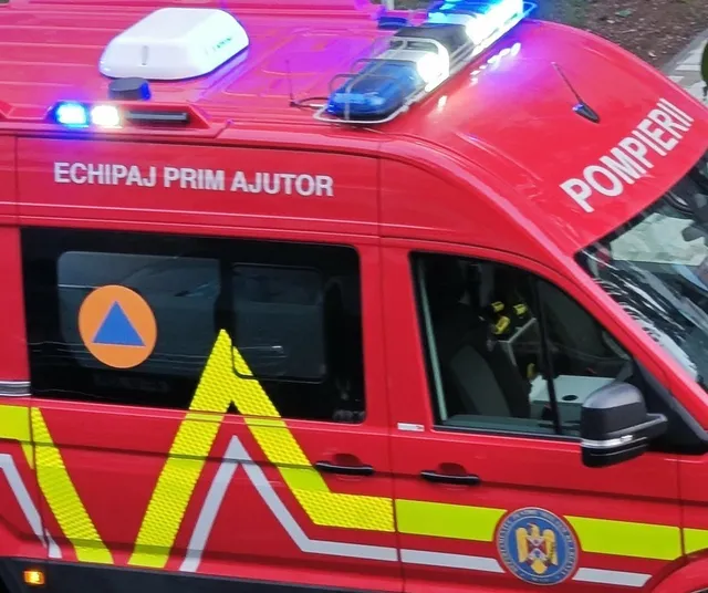 Un vehicul de serviciu de culoare roșie prezintă inscripții albe și lumini de semnalizare albastre aprinse pe plafon.