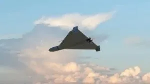O dronă cu aripi în formă de triunghi zboară pe un cer cu nori difuși.