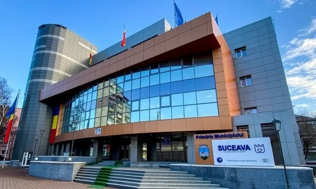 O clădire modernă cu fațadă de sticlă și panouri gri prezintă un panou informativ cu textul SUCEAVA în partea dreaptă jos.
