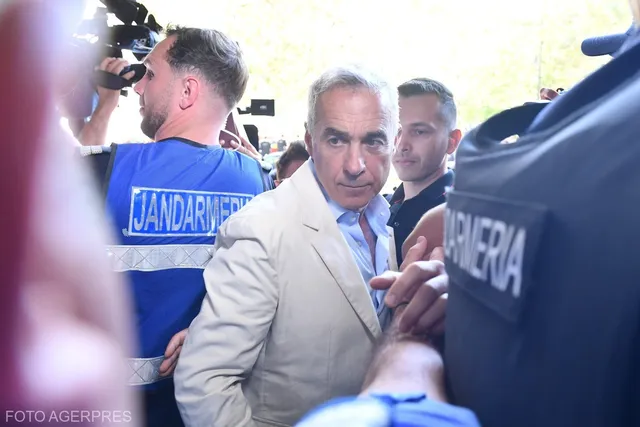 Un bărbat într-un sacou deschis este înconjurat de persoane, inclusiv un oficial în uniformă albastră cu inscripția Jandarmeria pe spate.