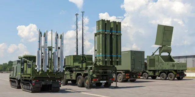 Patru vehicule militare verzi sunt parcate pe o suprafață asfaltată sub un cer cu nori, transportând rachete și echipamente tehnice.