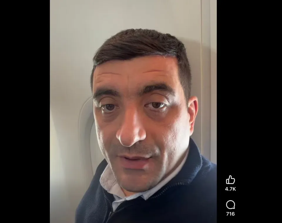 Un bărbat cu părul scurt și pielea deschisă poartă un hanorac albastru peste o cămașă albă.