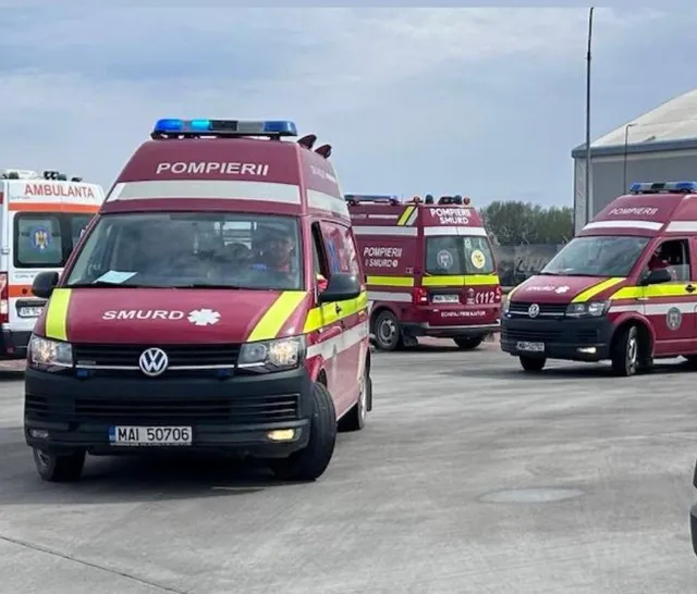 Trei ambulanțe de culoare roșie cu inscripții de serviciu sunt parcate pe o suprafață asfaltată sub un cer înnorat.