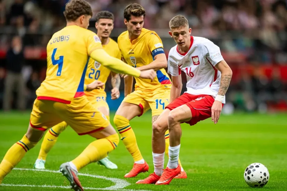 Câțiva jucători de fotbal în echipamente galbene și unul în echipament alb și roșu dispută un meci pe un teren de iarbă verde.